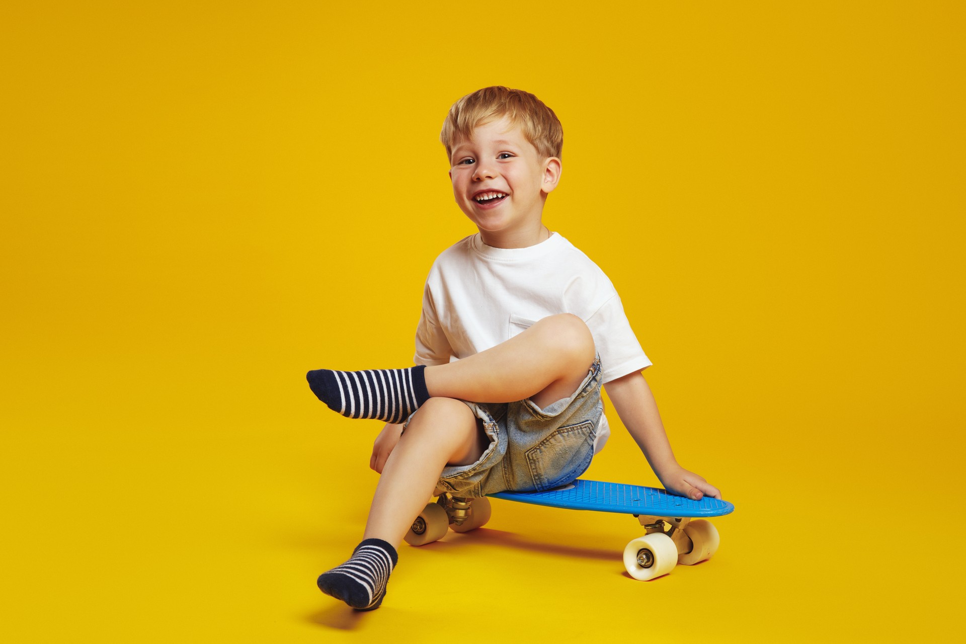 Happy child boy in white tshirt smiling and looking at camera while sitting on modern skateboard